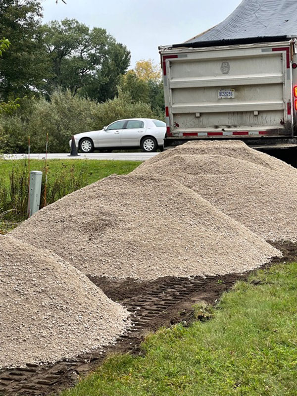 Three piles of gravel in preared driveway with dump truck pouring